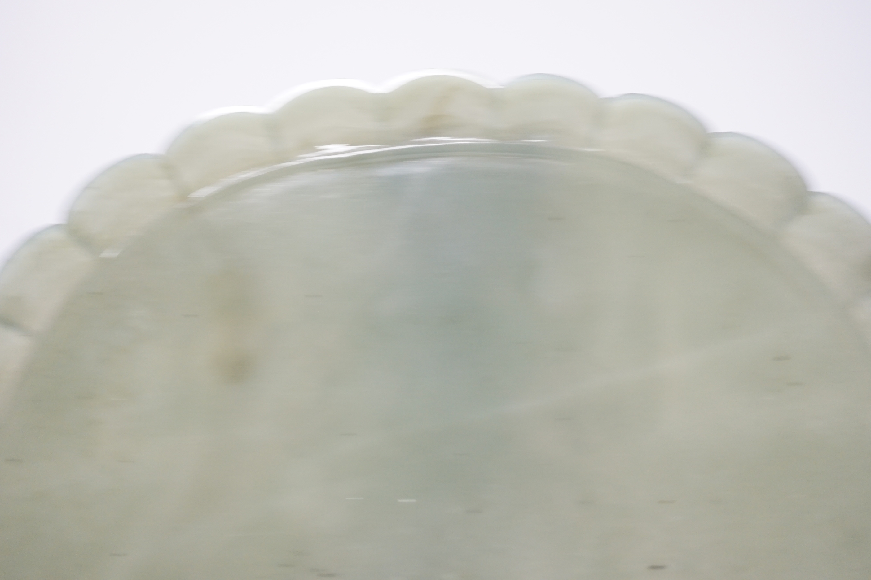 A Mughal style oval celadon jade dish, with petal lobed rim the underside carved with leaves, wood stand, 20cm